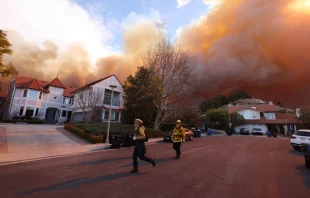 Firefighters run as a brush fire burns in Pacific Palisades, California, on Jan. 7, 2025. A fast-moving brushfire in a Los Angeles suburb burned buildings and sparked evacuations as “life-threatening” winds whipped the region. Credit: David Swanson/AFP via Getty Images