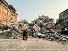 People stand past the debris of a collapsed building in Mandalay, Myanmar, on March 28, 2025, after a powerful earthquake killed more than 150 people across Myanmar and Thailand on March 28, toppling buildings and bridges and trapping over 80 workers in an under-construction skyscraper in Bangkok.