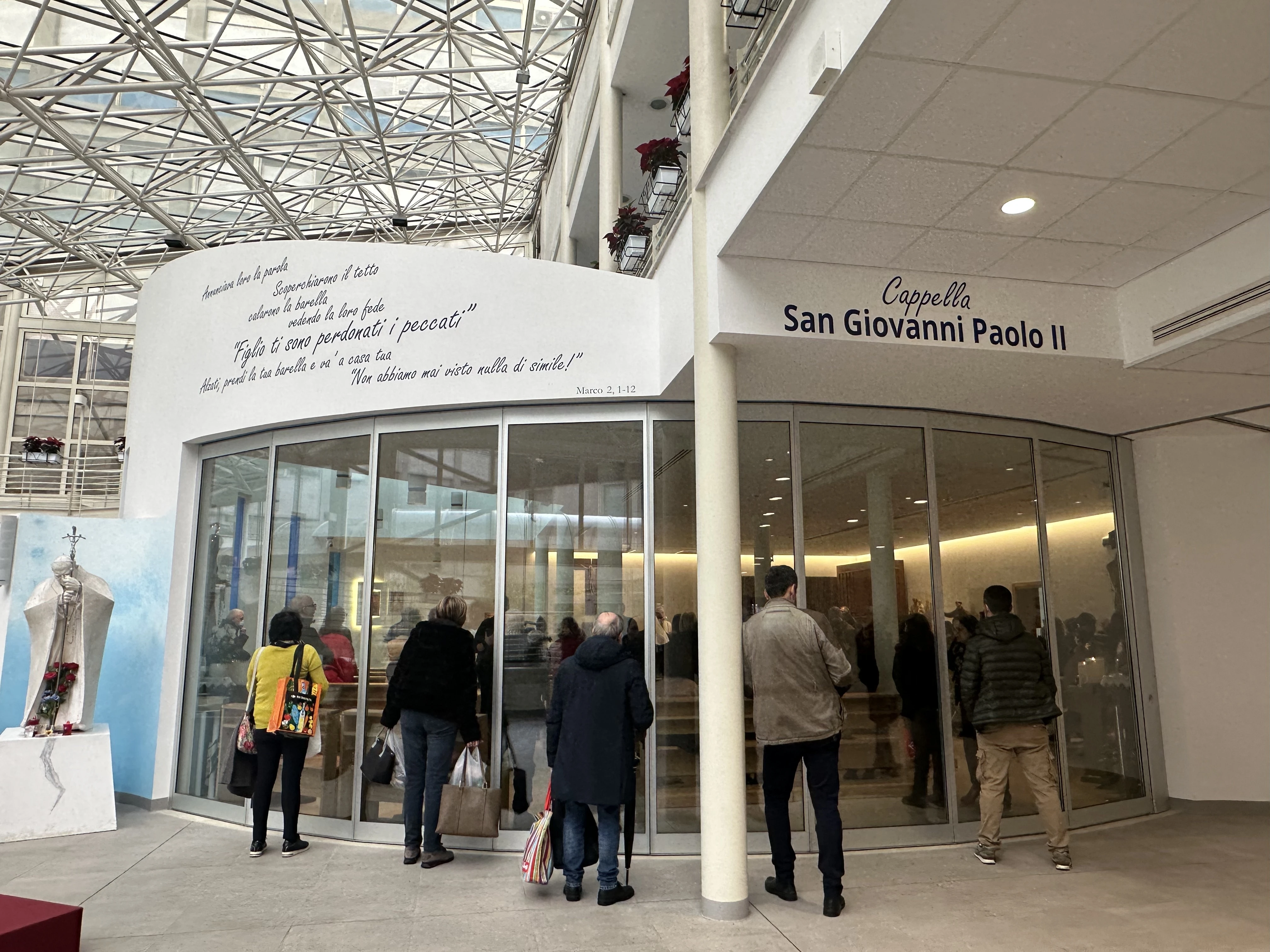 Passersby peer into the John Paul II Chapel at Gemelli Hospital in Rome, where a daily Holy Hour is among several prayer initiatives in the Eternal City for the health and recovery of Pope Francis. Credit: Courtney Mares/CNA