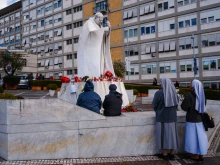 People pray at the statue of John Paul II outside Gemelli Hospital in Rome, where Pope Francis is hospitalized with pneumonia, on Feb. 27, 2025.